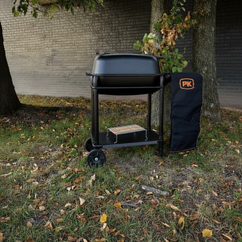 PK Grills The Exclusive AmazingRibs.com PK300 Bundle - Graphite, outdoor charcoal grill with a cover and stand, placed on a grassy area next to trees.