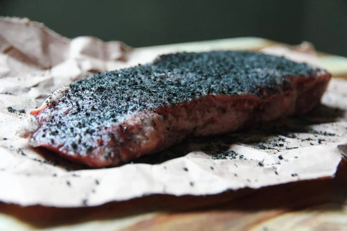 Hardcore Carnivore - Black Seasoning, raw steak with black seasoning on top, ready to be cooked, on parchment paper.