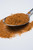 Fire & Smoke Society F&S | Pork Perfect Spice Rub 10.7 oz, close-up of a metal spoon filled with a reddish-brown spice rub, with some spilled on a white surface.