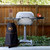 PK Grills PK360 Start Cookin' Bundle - Silver, outdoor barbecue grill with side shelves, thermometer, and accessories, set against a wooden fence background.