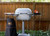 PK Grills PK360 Start Cookin' Bundle - Silver, outdoor grill with side shelves, thermometer, and accessories, set against a wooden fence with greenery.