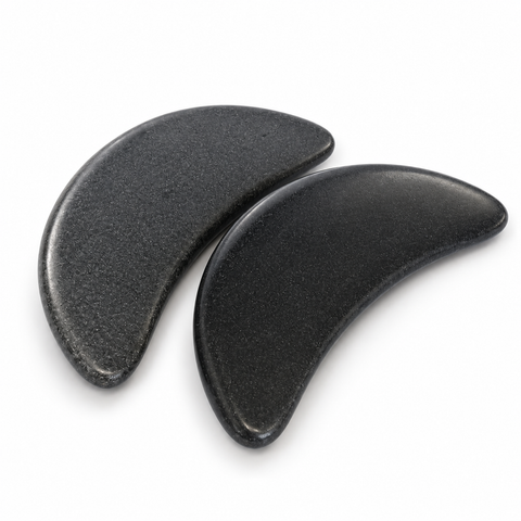 Two natural black crescent basalt massage stones with contoured edges for professional Gua Sha and hot stone massage treatments.