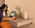 Denon Home 200 – Wireless Smart Speaker with HEOS® stone with an asian lady doing work at a desk