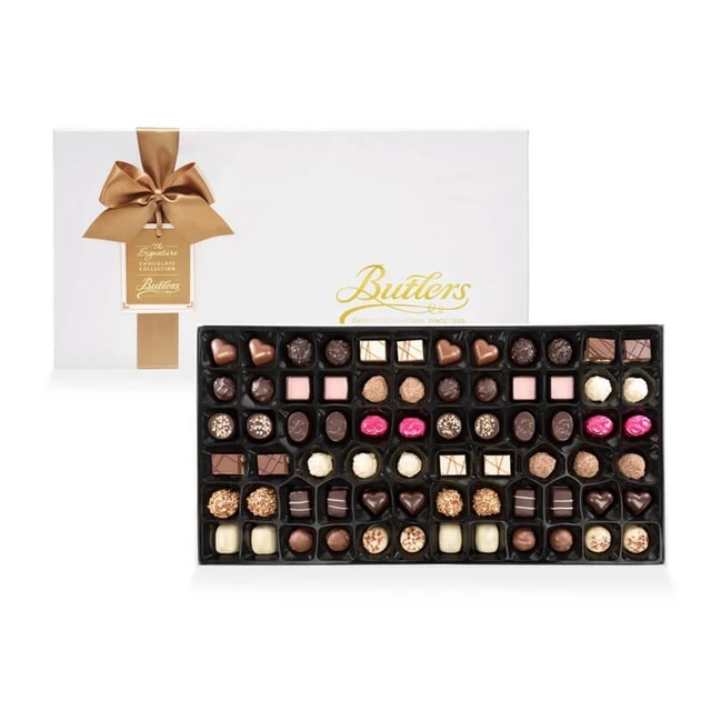 Butlers Luxury Chocolate Assortment 1000G: A white box of chocolates adorned with a gold ribbon and tag is partially open, revealing an assortment of chocolates arranged neatly inside. The interior features a variety of shapes and colors, including dark, milk, and white chocolate pieces.