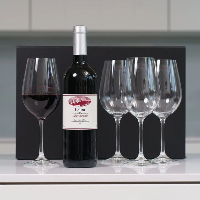Personalised Wine & Crystal Glasses gift set featuring custom-labeled birthday wine bottle for 'Laura', four elegant crystal glasses—one filled with red wine—arranged in front of a black gift box.
