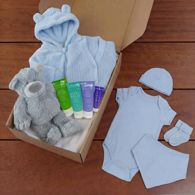 Luxury blue baby gift set in a gift box with hooded jacket, knitted cardigan, bodysuit, hat, socks, teddy bear and baby skincare products.