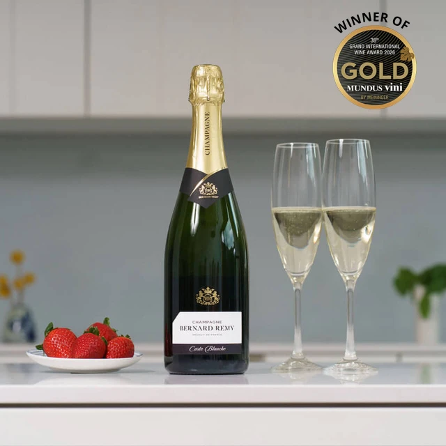 Champagne Bernard Remy Gift Box. A bottle of champagne is displayed on a kitchen counter next to two filled Champagne flutes. A plate of fresh strawberries sits nearby, adding a pop of color to the scene. The background features muted tones and soft lighting, creating an inviting atmosphere.