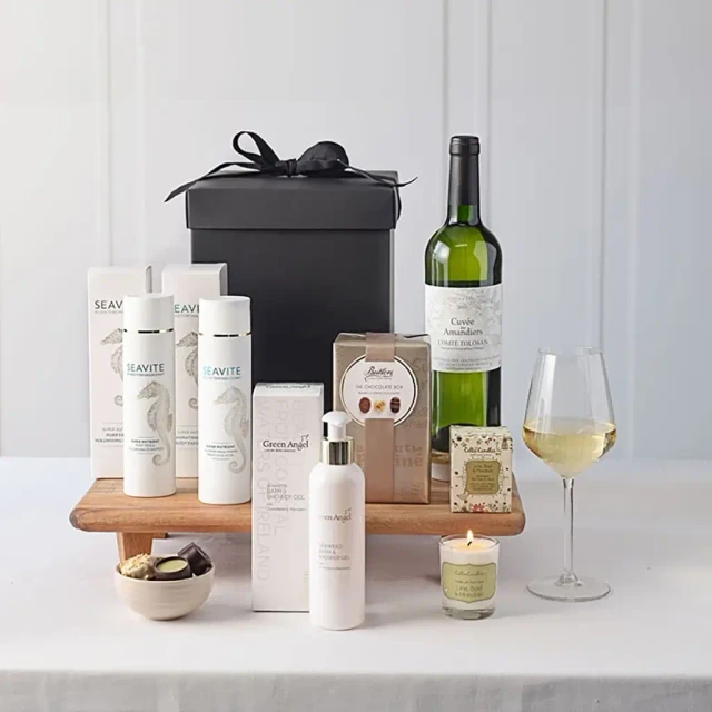 Ultimate Relaxation Pamper Gift with luxury skincare products, scented candle, gourmet chocolates, and a bottle of white wine in an elegant black gift box – available at GiftsDirect.com