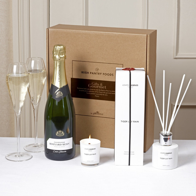 Luxury Champagne Relaxation Gift Box. A gift box from Irish Pantry Foods containing a bottle of champagne, a scented candle, and a fragrance diffuser. The items are arranged on a white table in front of a neutral backdrop.
