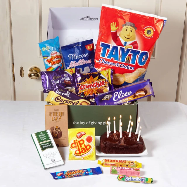 Its Your Birthday Treat Box: A gift box filled with various snacks, including Tayto crisps, chocolate bars like Dairy Milk and Crunchie, and candies such as Starburst. A chocolate cake with candles is placed in front of the box.