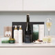 Ultimate Relaxation & Bubbles Pamper Hamper. A selection of luxury beauty and wellness products arranged on a countertop. Items include a large bottle of prosecco, two white bottles of lotion, a moisturizer, a box of chocolates, a candle, and various skincare product boxes. A glass of champagne is placed on the right. The background features light-colored cabinetry. Ultimate Relaxation & Bubbles Pamper Hamper. A selection of luxury beauty and wellness products arranged on a countertop. Items include a large bottle of prosecco, two white bottles of lotion, a moisturizer, a box of chocolates, a candle, and various skincare product boxes. A glass of champagne is placed on the right. The background features light-colored cabinetry.