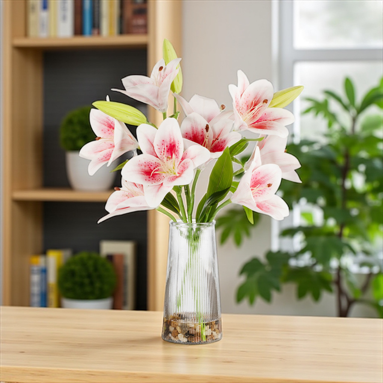 Pink real touch artificial tiger lily flower arrangement in a clear glass vase with faux water and river rock, styled on a wooden table in a bright home interior.