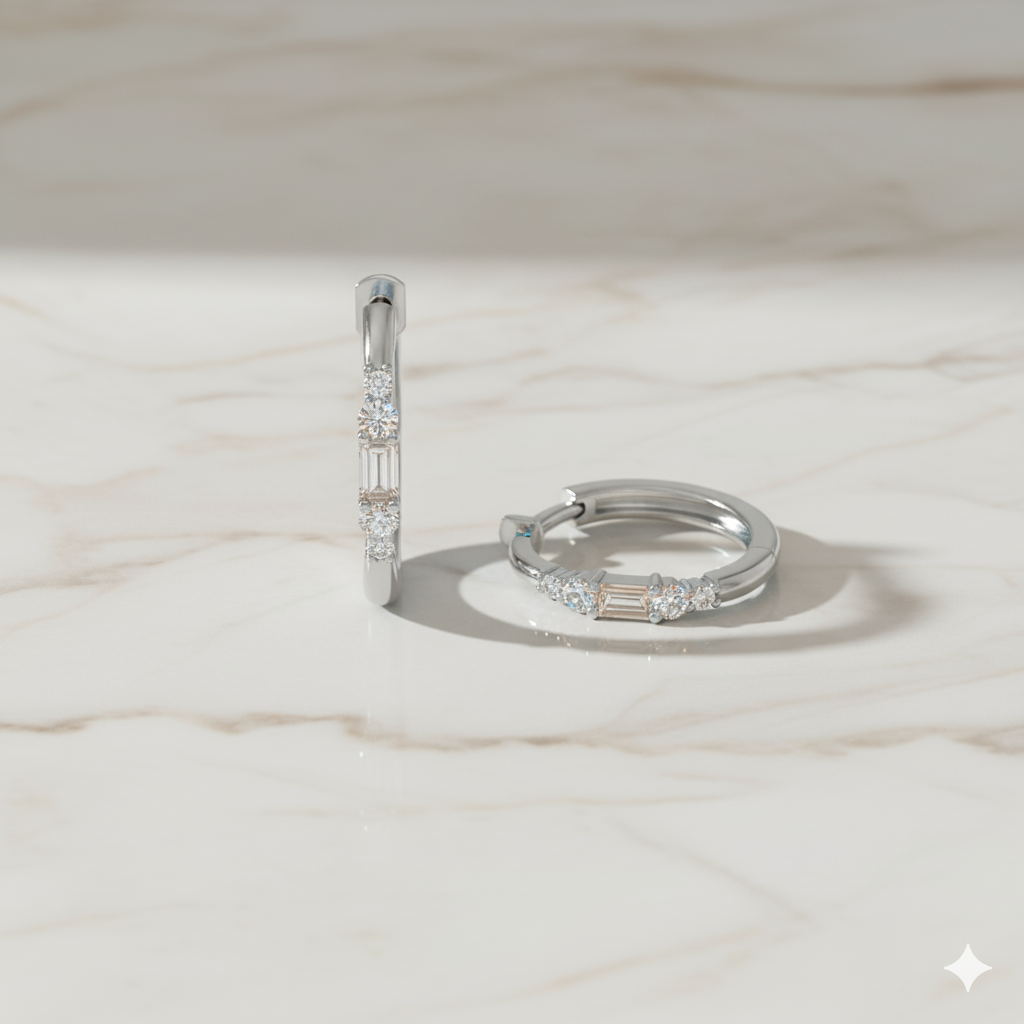 A front and top down view of a pair of 14K white gold huggie hoops, showcasing the baguette and round diamonds on a marble background.