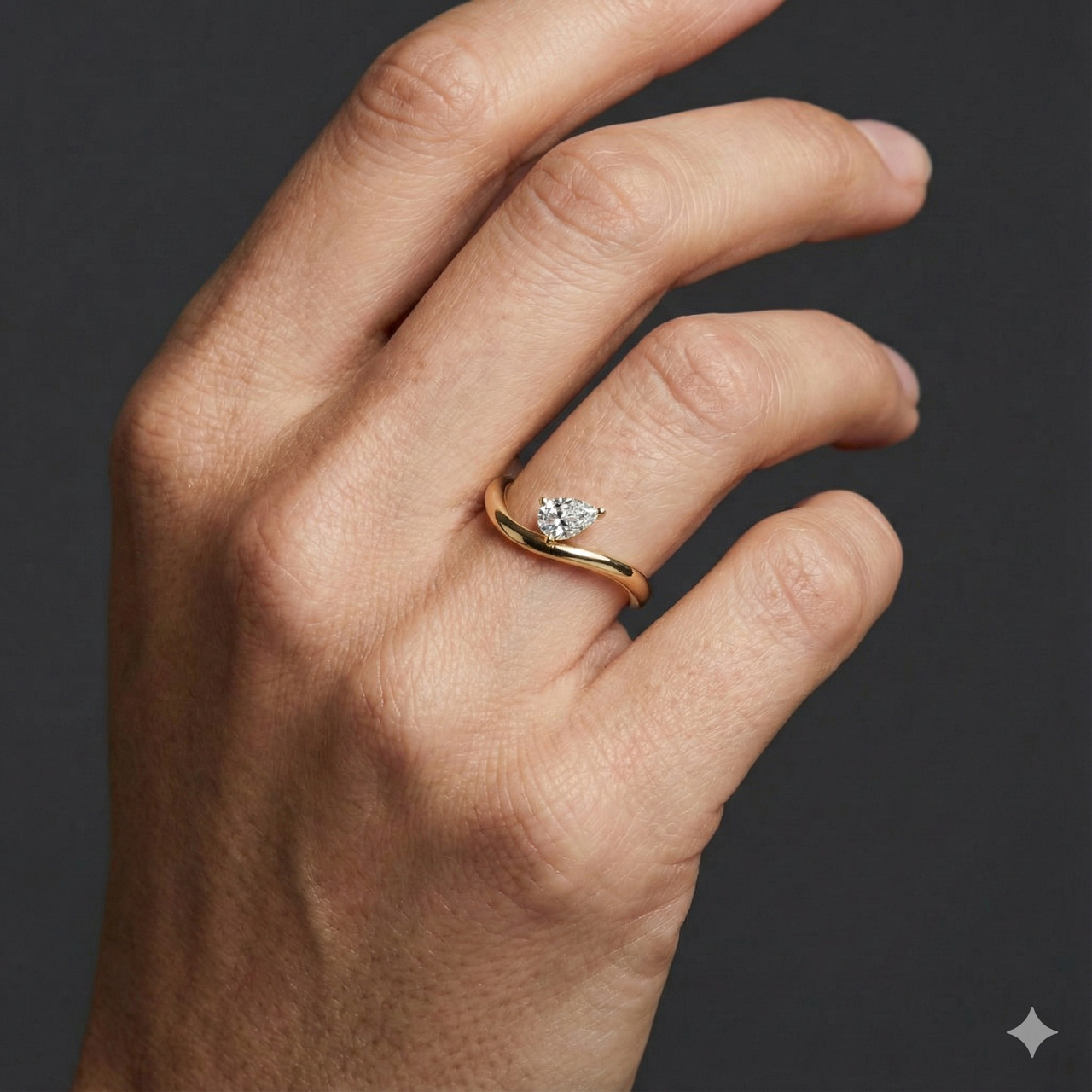 Close-up of a hand wearing a minimalist 14k yellow gold diamond ring featuring a single pear-cut diamond set on a slim, gently curved band, photographed against a dark background to highlight delicate sparkle and modern elegance.