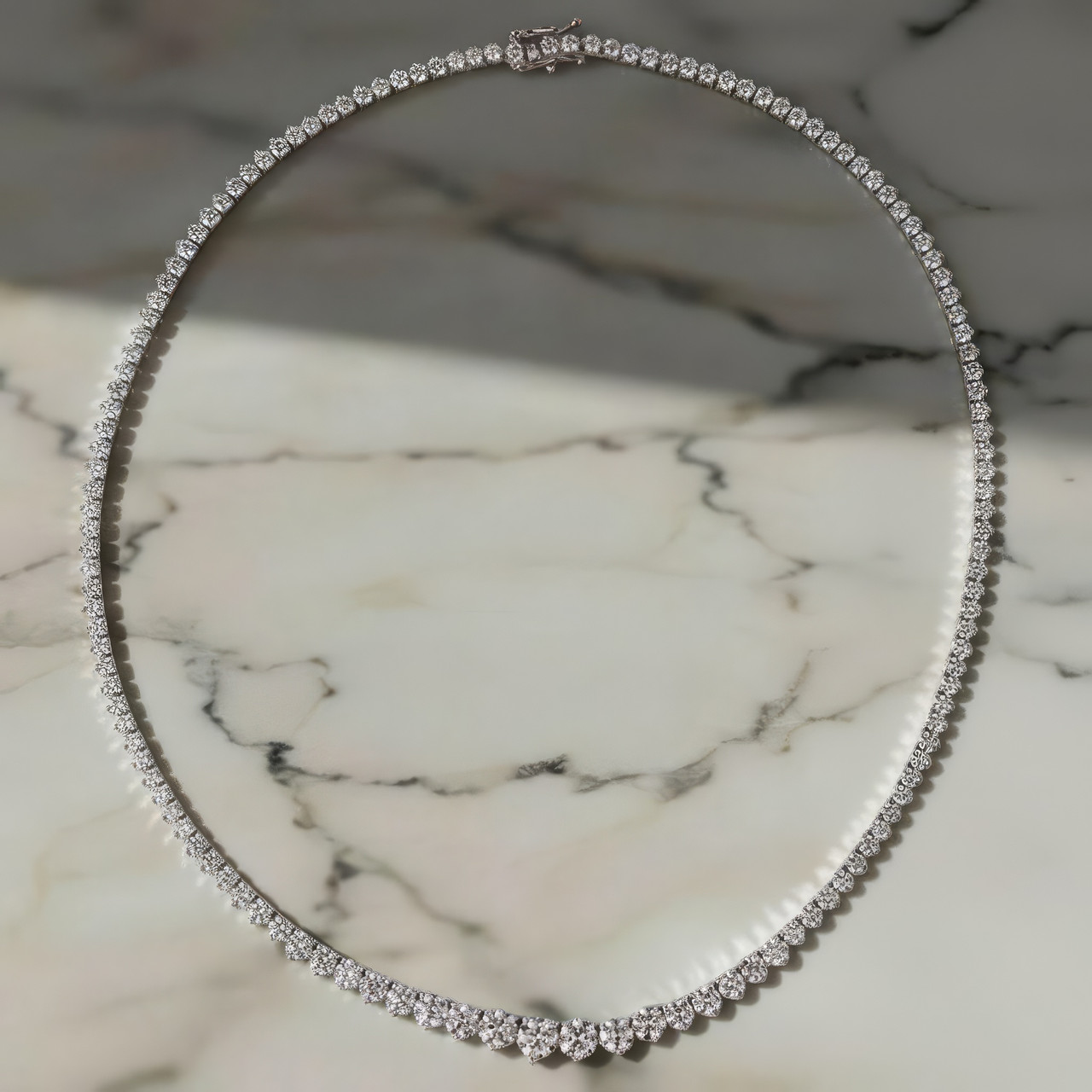 White gold diamond tennis necklace resting on marble, highlighting clean lines, polished metal, and continuous diamond sparkle.
