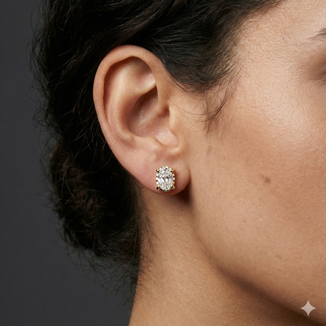 Yellow gold oval solitaire diamond stud earrings worn on ear, delivering a warm glow and understated everyday elegance.