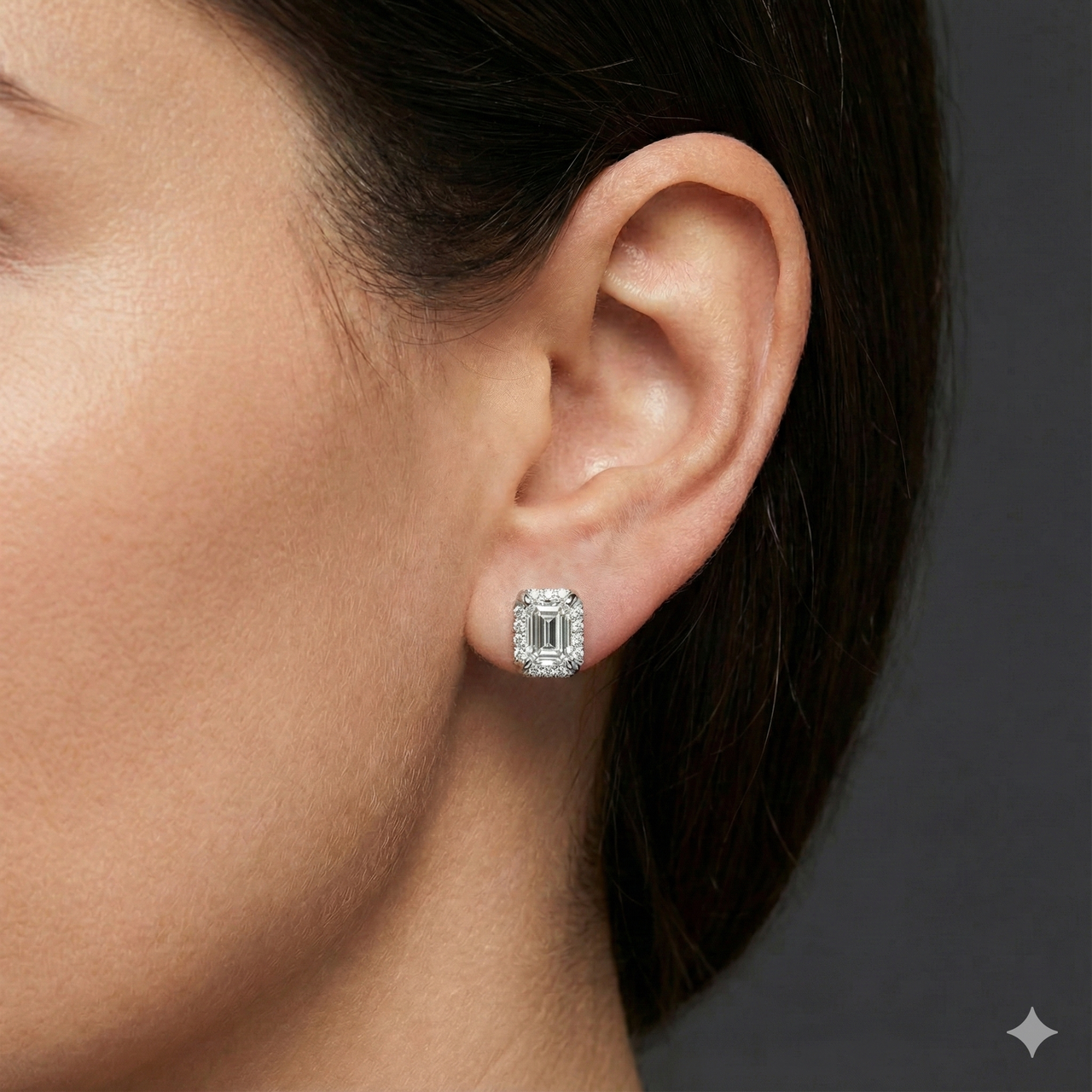 White gold emerald-cut halo diamond stud earrings worn on ear, displaying a crisp, modern silhouette with elegant brilliance.