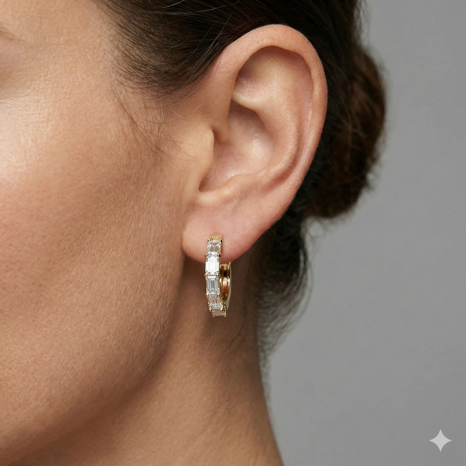 A pair of 14K yellow gold huggie hoops with a continuous line of horizontal baguette diamonds, shown from the front on ear.