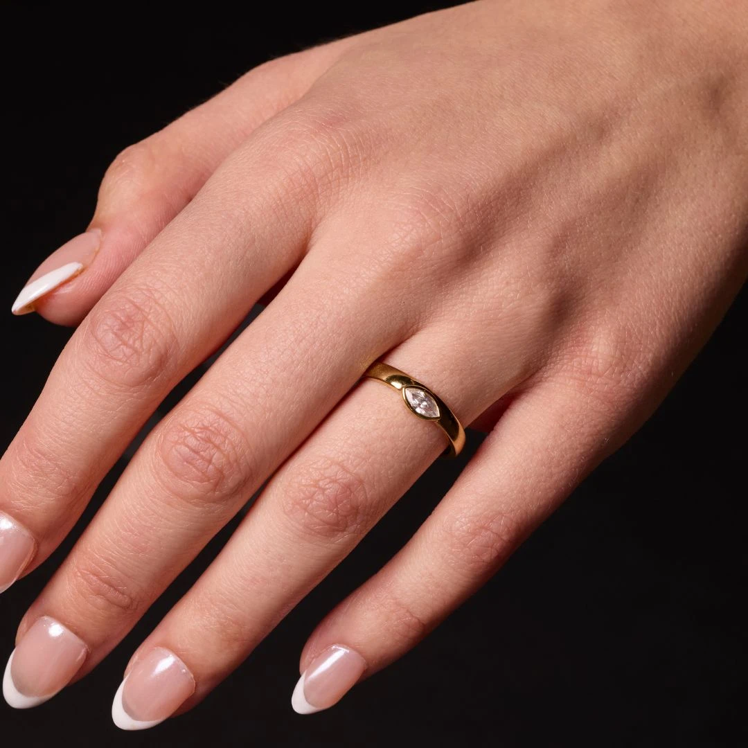 On hand view of a 14K yellow gold bypass ring with a single, bezel-set round diamond in a fluid, curving band on marble