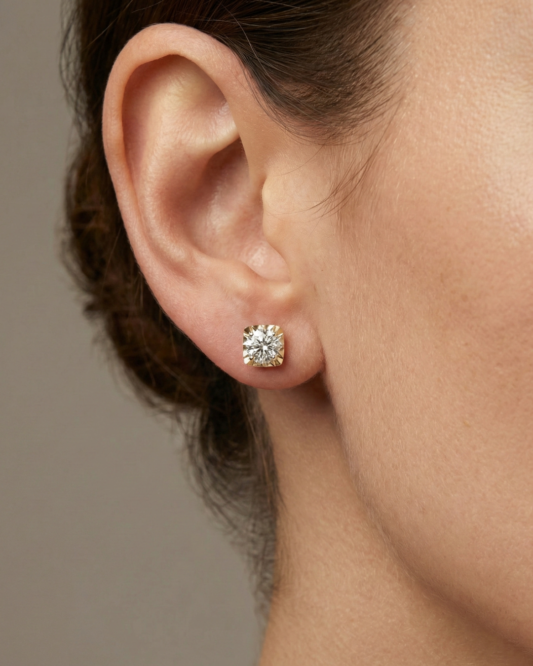 A pair of 14K yellow gold classic stud earrings with round diamonds, shown from the front on ear.