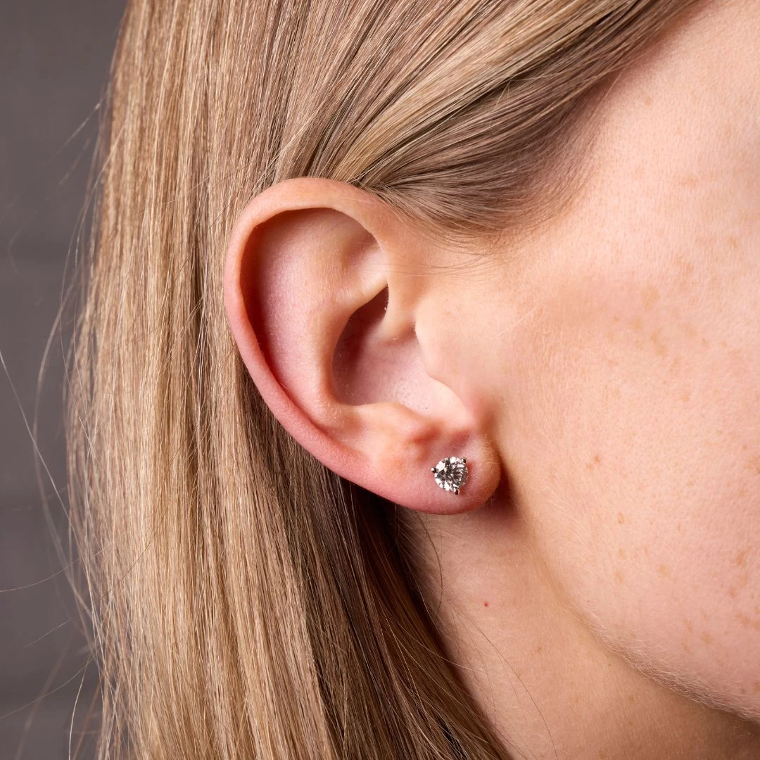 An on model view of a 14K white gold three-prong .24 ct total weight diamond stud earrings, shown on the left ear.