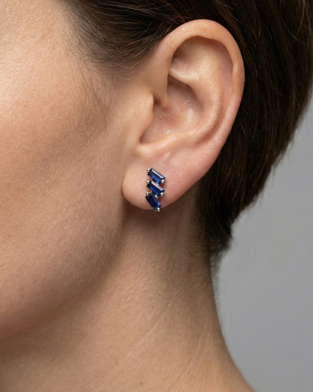 A close-up, profile shot of a person’s ear and jawline, showcasing the Cascading Baguette-Cut Stud Earrings. The model’s hair is swept back, allowing the jewelry to take center stage against a soft-focus, neutral background.