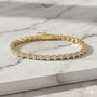 Lifestyle view of a 14K yellow gold tennis bracelet, coiled to show the seamless path of framed round diamonds on a marble background.