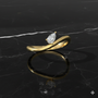 A top-down view of a 14K yellow gold bypass ring with a single pear-shaped diamond at one end of a fluid, curving band on marble.