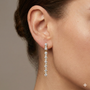 A pair of 14K yellow gold vertical drop earrings, shown from the front with a continuous line of brilliant round diamonds on ear.