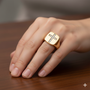 An angled view of a 14K yellow gold signet ring, showcasing the pavé jewel cross design on a hand.