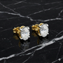 Yellow gold oval solitaire diamond stud earrings styled on black marble, highlighting rich gold color and clean diamond sparkle.