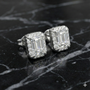 White gold emerald-cut halo diamond stud earrings photographed on black marble, emphasizing sharp geometry, contrast, and luxury sparkle.