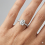 Emerald cut diamond engagement ring in 14k white gold with a pavé diamond band and cathedral setting on a hand