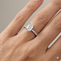 Emerald cut diamond engagement ring in 14k white gold with a prong diamond band and cathedral setting on a hand