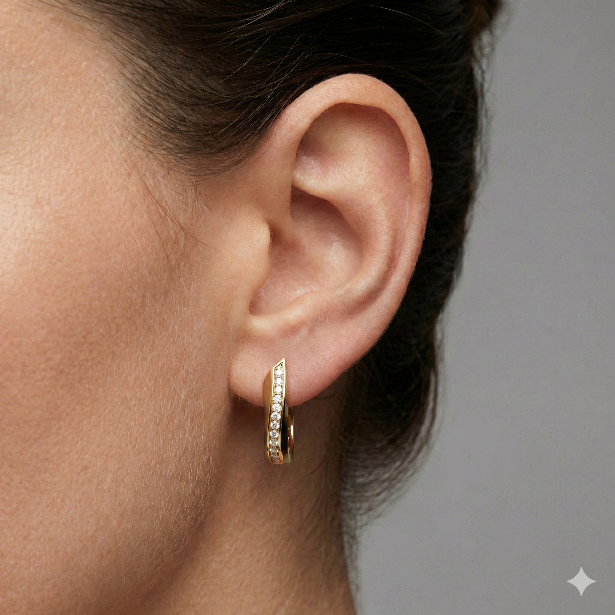 A pair of 14K yellow gold huggie hoops with a diagonal line of pavé diamonds, shown from the front on ear.