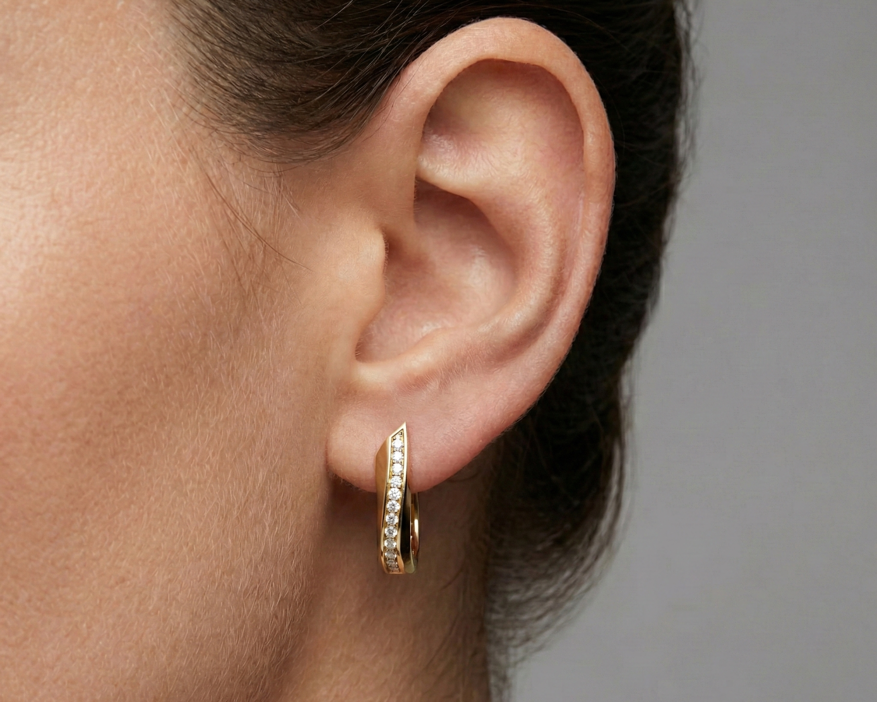 A pair of 14K yellow gold huggie hoops with a diagonal line of pavé diamonds, shown from the front on ear.