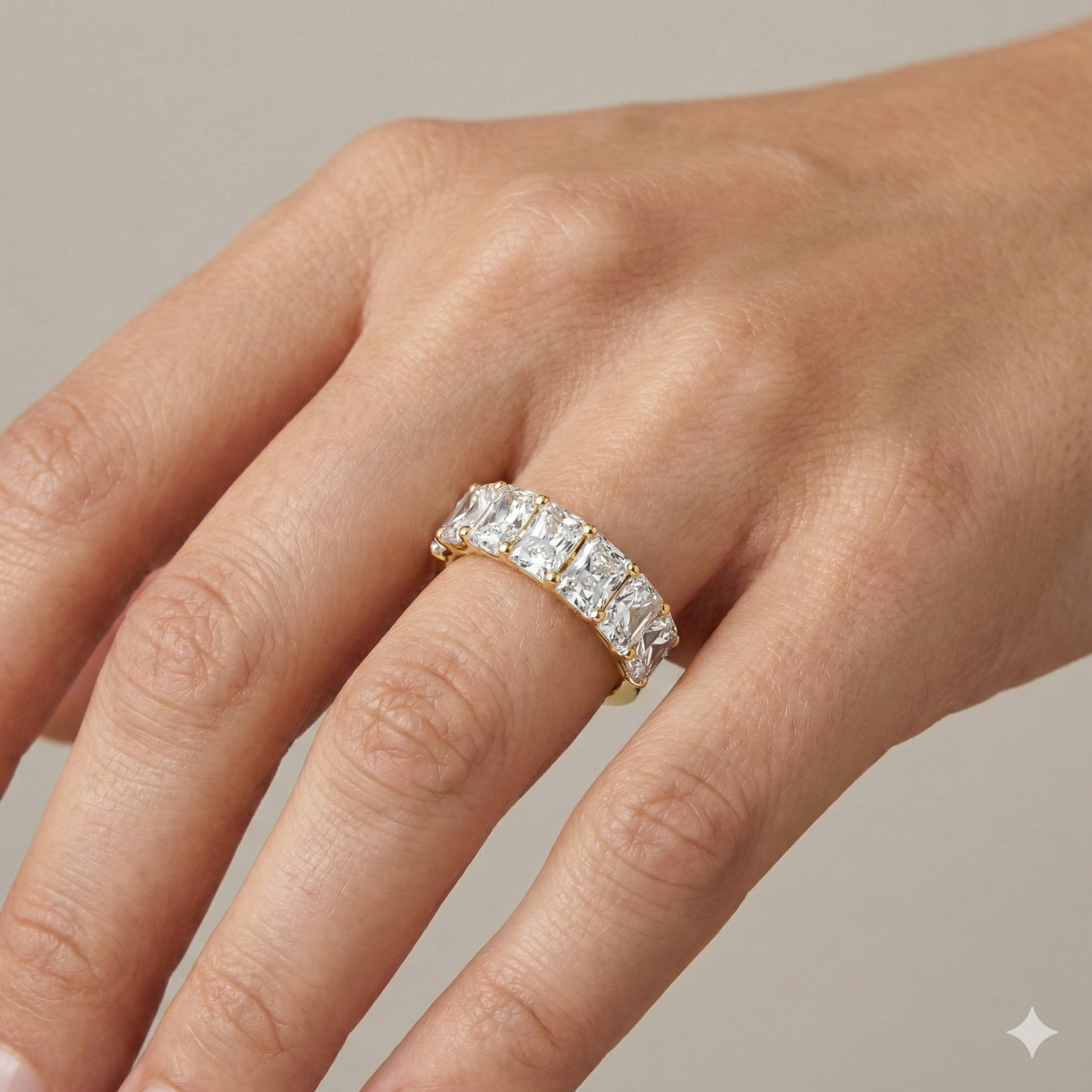 A top-down view of a 14K yellow gold wide band ring with five horizontally-set emerald-cut diamonds on hand.