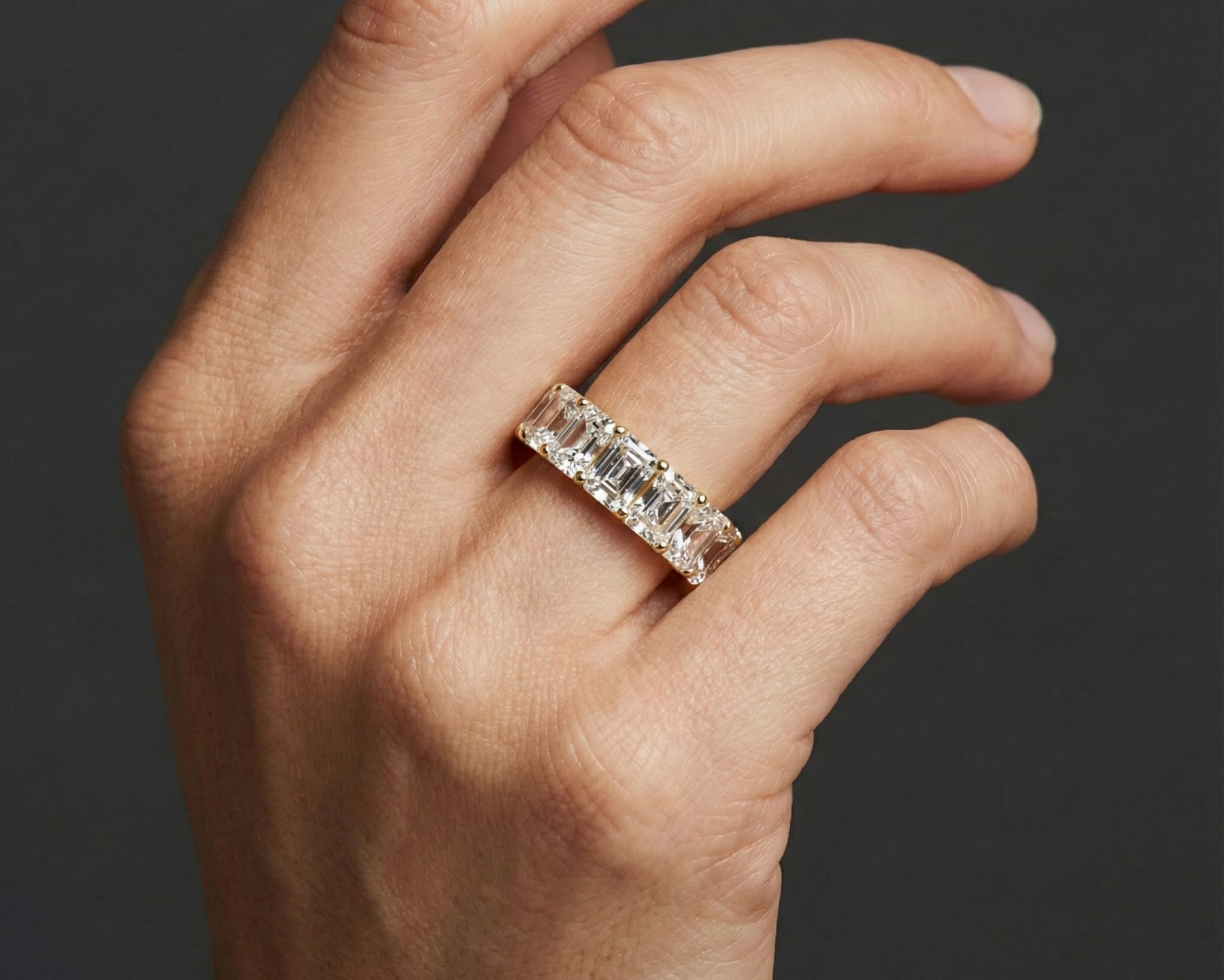A top-down view of a 14K yellow gold wide-band ring with five horizontally set emerald-cut diamonds on hand.