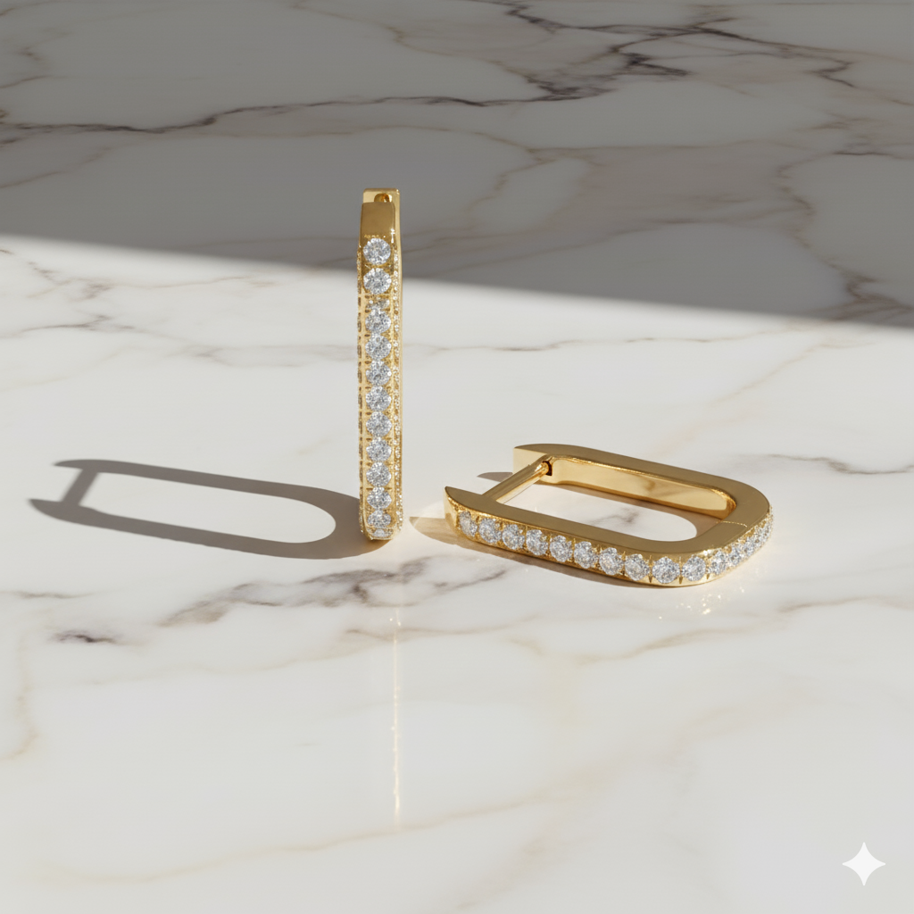 A pair of 14K yellow gold rectangular huggie hoops, shown from the front and top down with a pavé diamond surface and rounded corners on a marble background.