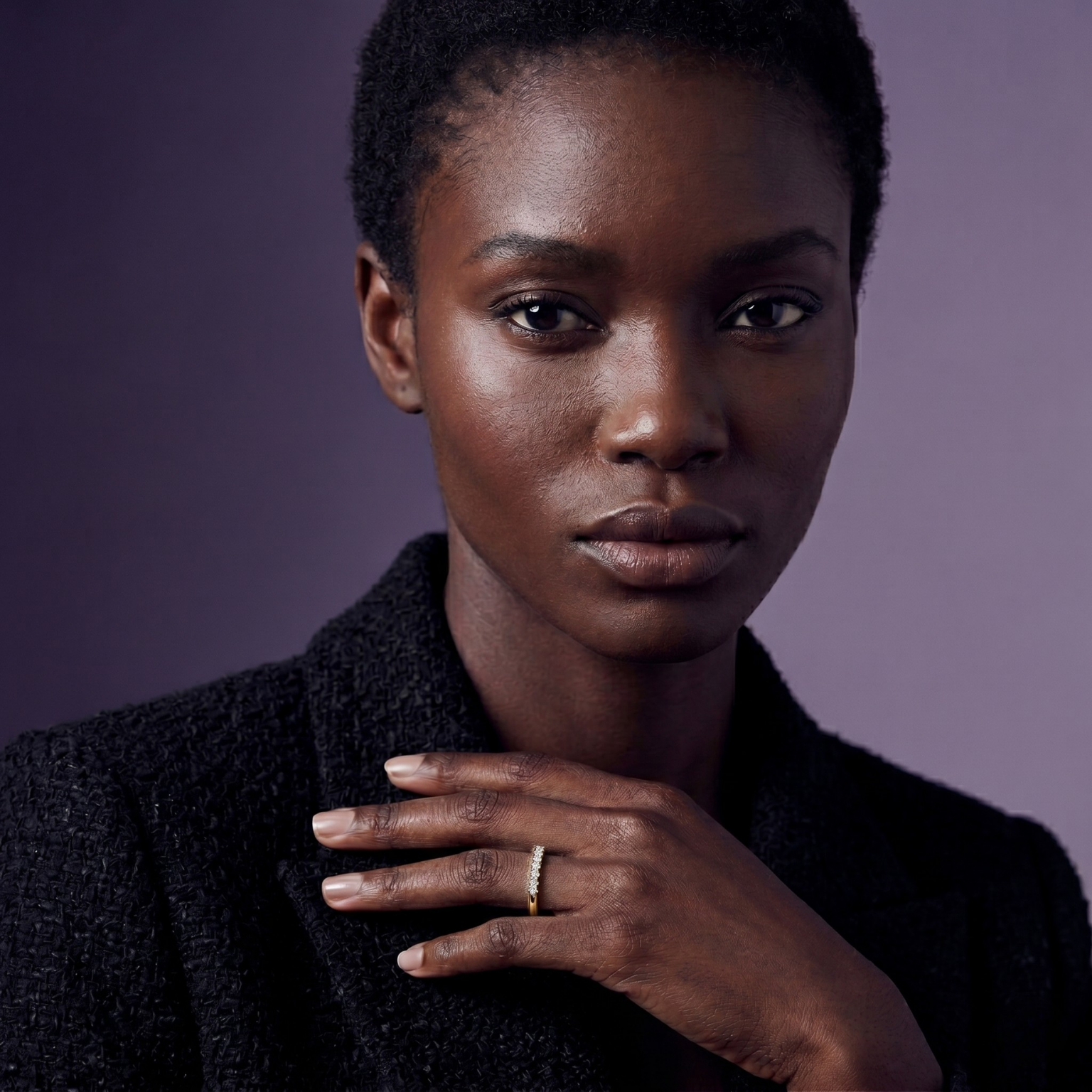 Model wearing a delicate gold ring with a row of small diamonds, styled with a black tweed blazer against a purple backdrop.
