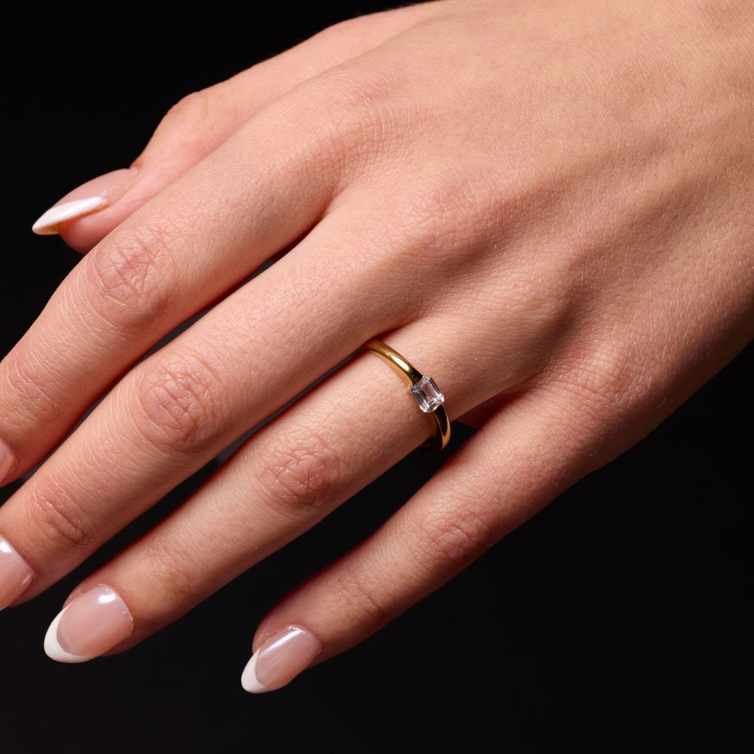 On hand view of a 14K yellow gold ring with a series of horizontal, square-cut diamonds laying on a marble background.
