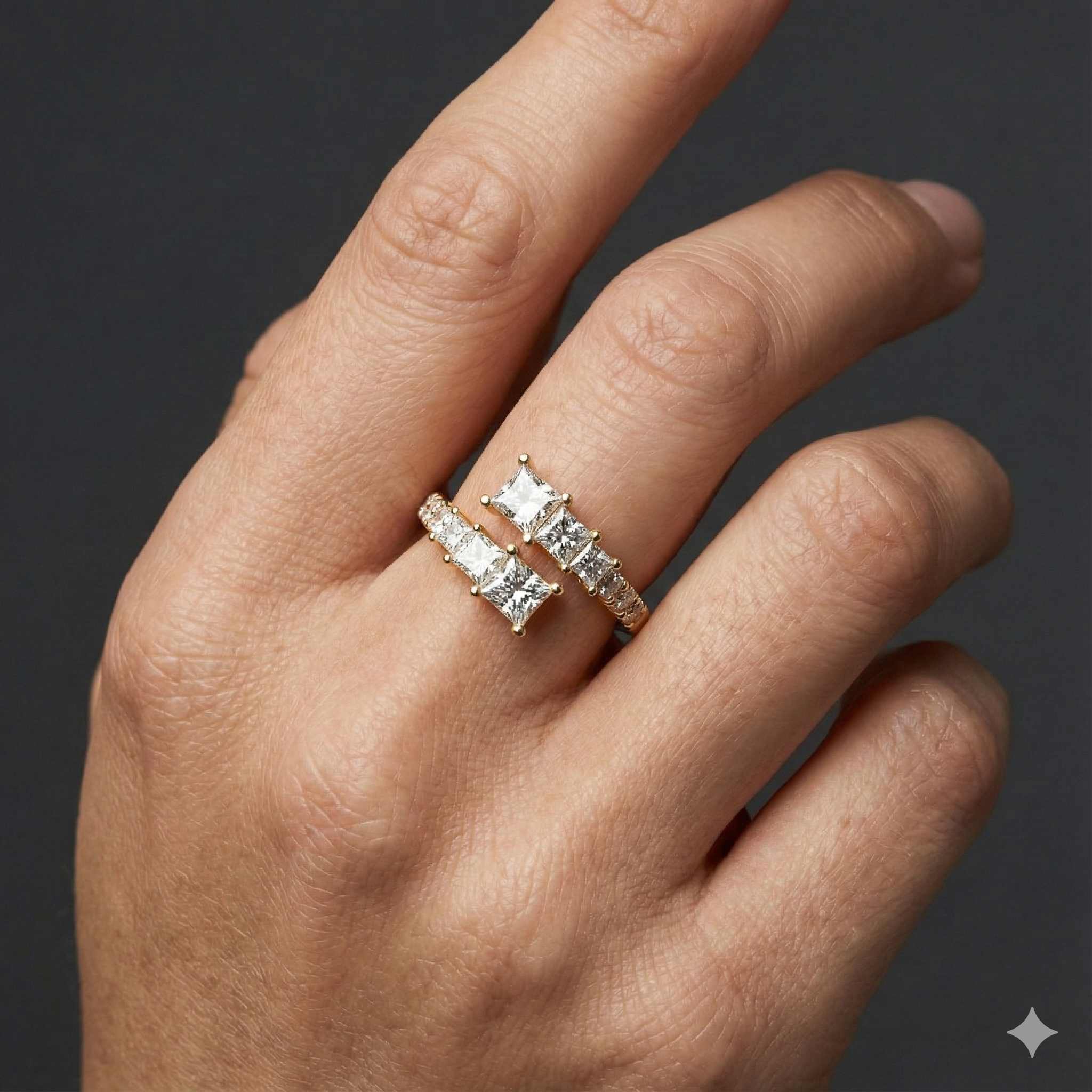 Close-up of a hand wearing a 14k yellow gold open diamond ring featuring princess-cut diamonds set across a modern, split-band design, photographed against a dark background to highlight clean lines, refined sparkle, and contemporary elegance.
