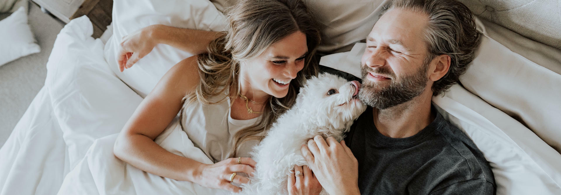 a man, woman, and dog sitting on a bed with Cariloha sheets