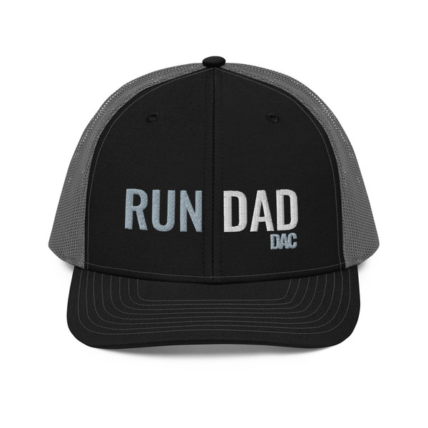 Black/Charcoal six-panel snapback-style trucker cap with embroidered Run DAD logo, front view — DAD all caps