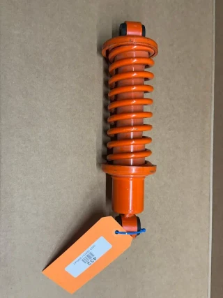 Allis Chalmers Seat Shock Absorber with Spring, orange suspension component for tractor seat, displayed on a beige background.