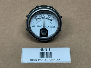Allis Chalmers Amp Gauge (60-0-60) 12 Volt, a round electrical gauge with a white face, black markings, and a needle indicating zero, used for measuring electrical current in amps, displayed on a brown background.