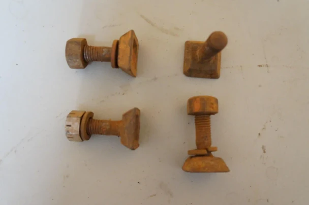 A collection of four rusty bolts with square or round heads, used for Allis-Chalmers farm tractors, resting on a light-colored surface.