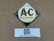 Allis Chalmers Cream Emblem Steering Wheel, display of a vintage metal automobile emblem with cream and black coloring, featuring the Allis Chalmers logo.