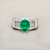 Oval emerald ring with prong-set centre and diamond halo close-up