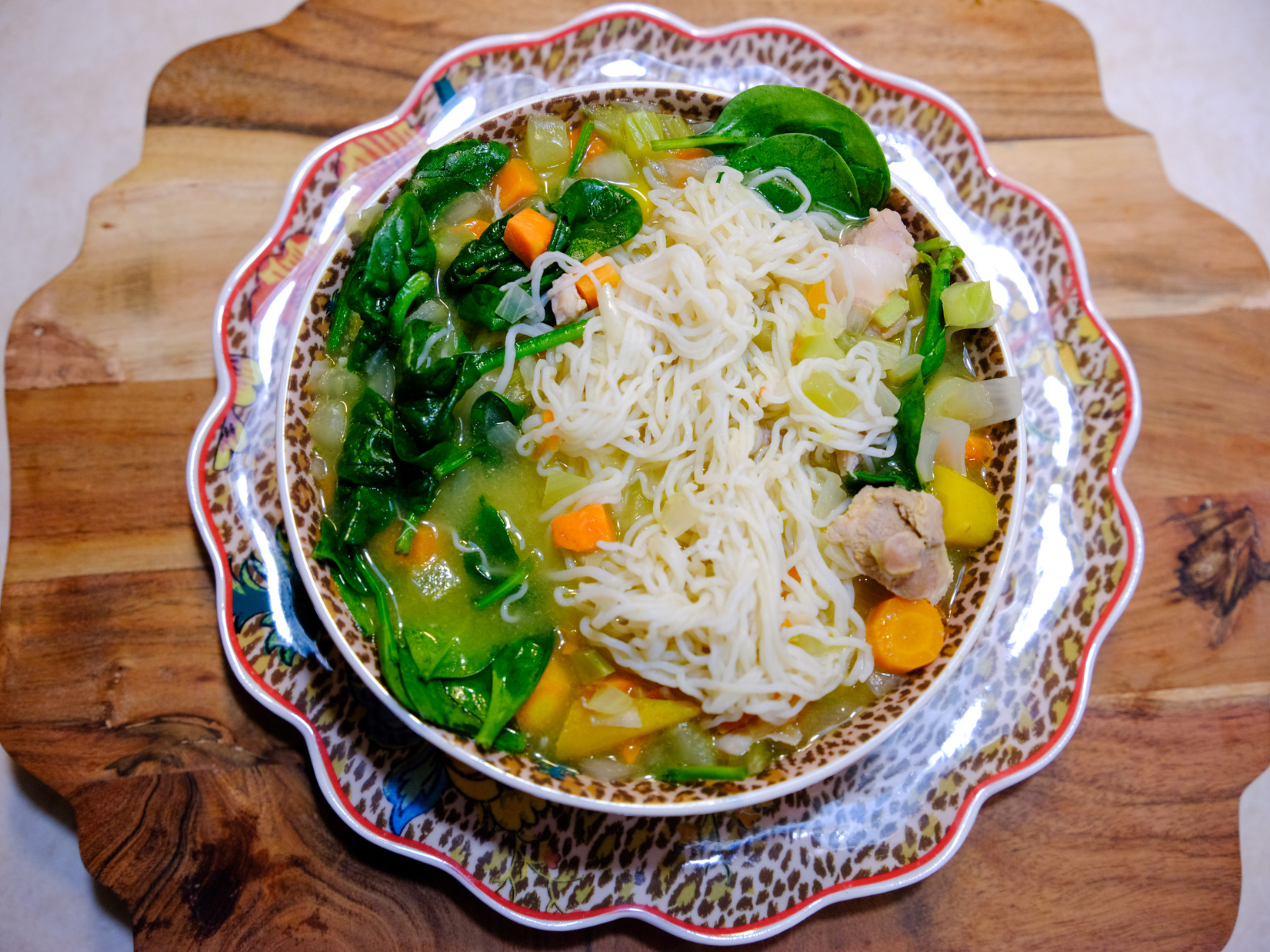 An overhead image of a large bowl of hearty, low-carb chicken noodle soup made with It's Skinny Angel Hair pasta, spinach, carrots, and more veggies in a rich broth.